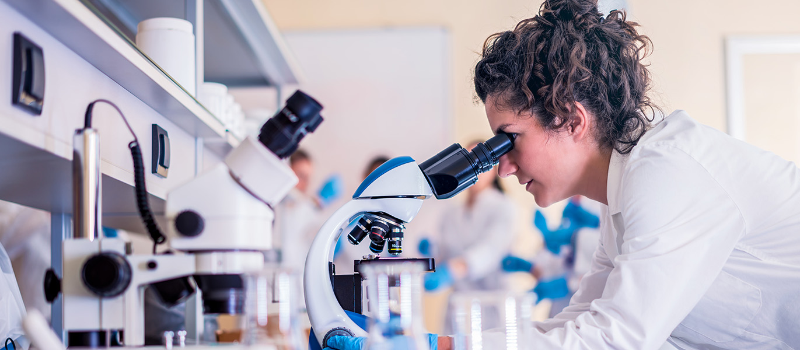 Female scientist looking into a microscope in a lab - courtesy Getty Images