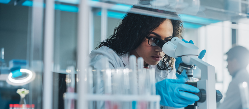 Photo of woman working in lab, looking into a microscope - Courtesy Getty images